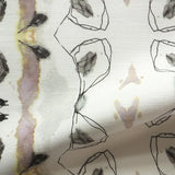 Detail of draped fabric yardage in a watercolor ikat stripe print in shades of gray, pink and yellow on a white field.