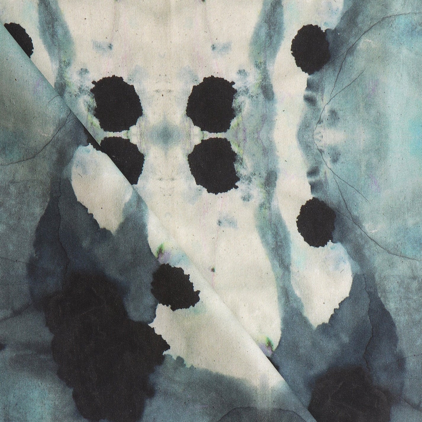 Close-up of draped fabric in a watercolor ink blot print in shades of charcoal and gray on a tan field.
