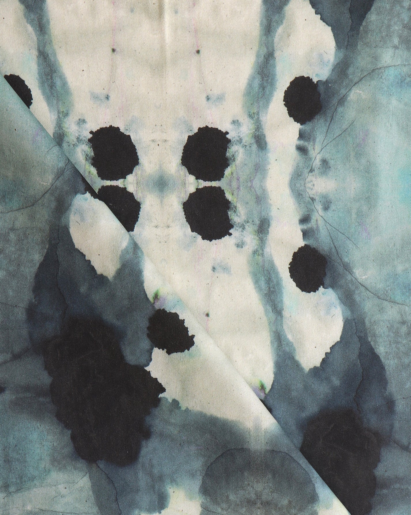 Close-up of draped fabric in a watercolor ink blot print in shades of charcoal and gray on a tan field.