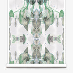 Partially unrolled wallpaper yardage in a watercolor paint blotch print in shades of gray and green on a white field.