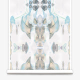 Partially unrolled wallpaper yardage in a watercolor paint blotch print in shades of gray, blue and tan on a white field.