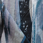 Draped fabric yardage in a watercolor paint print in shades of black, purple and blue on a gray field.