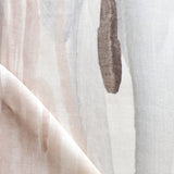 Draped fabric yardage in a watercolor paint print in shades of pink, brown and gray on a cream field.