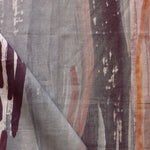 Draped fabric yardage in a watercolor paint print in shades of gray, orange and purple on a cream field.