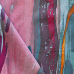 Draped fabric yardage in a watercolor paint print in shades of pink, purple and turquoise on a blue field.