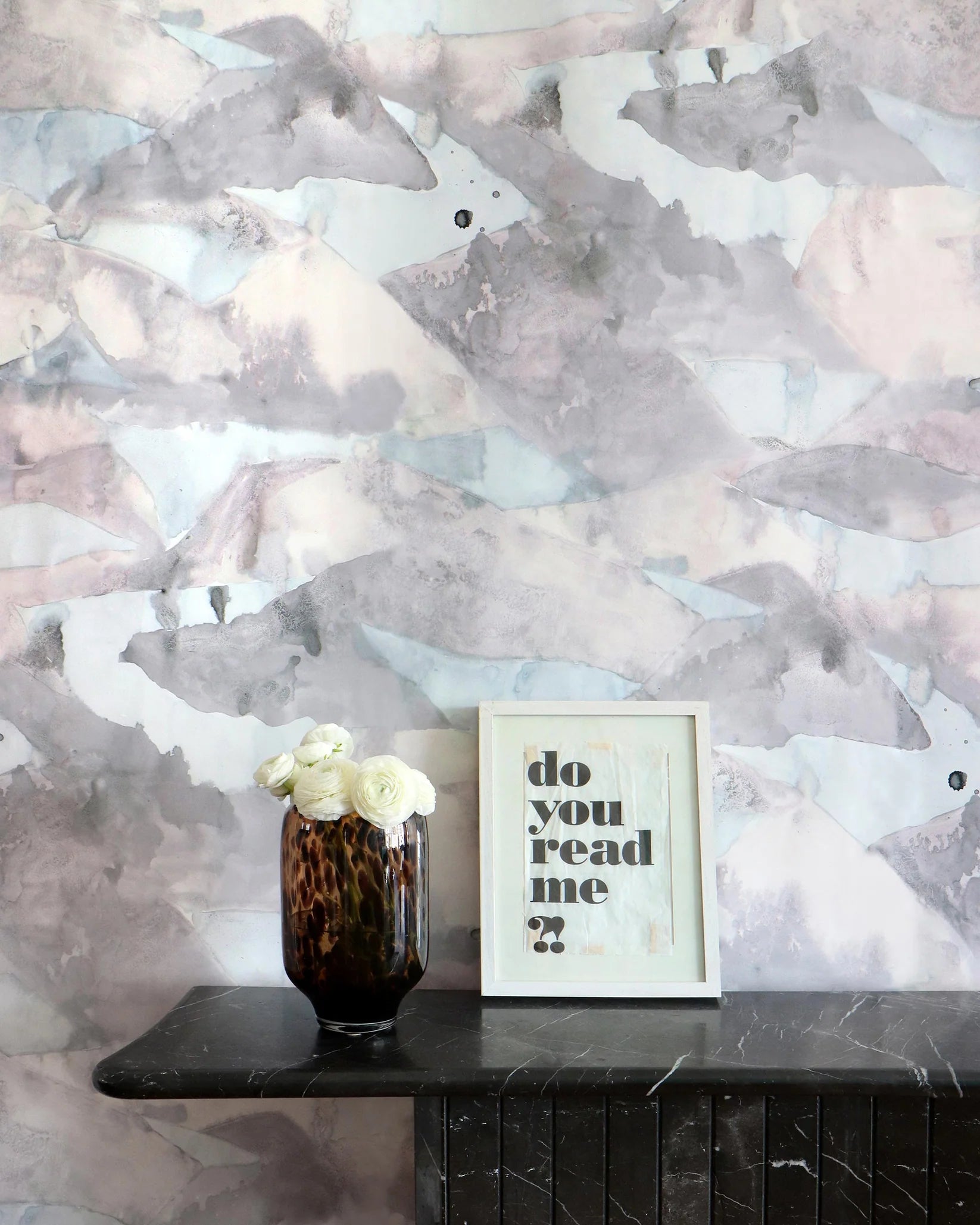 Decorative wall with abstract pattern, vase with flowers, and framed picture on a shelf.