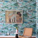 Room interior with a watercolor wallpaper in green and blue wall, wicker chair, and framed artwork.