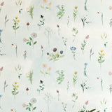 A vase of flowers stands in front of a wall covered in a painterly flower print in green and pastels on a cream field.