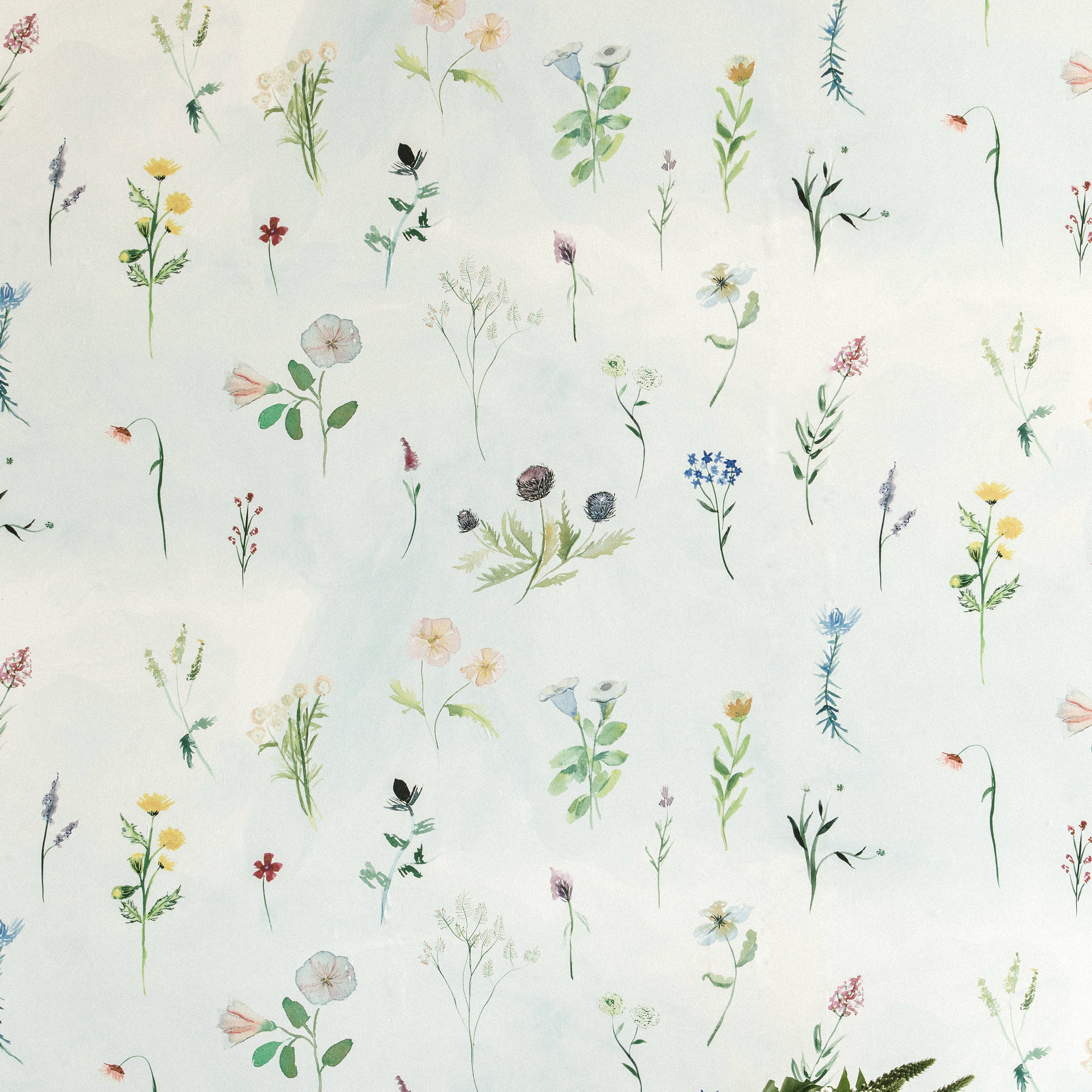 A vase of flowers stands in front of a wall covered in a painterly flower print in green and pastels on a cream field.