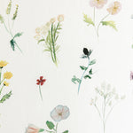 Detail of wallpaper in a painterly flower print in green and pastels on a cream field.