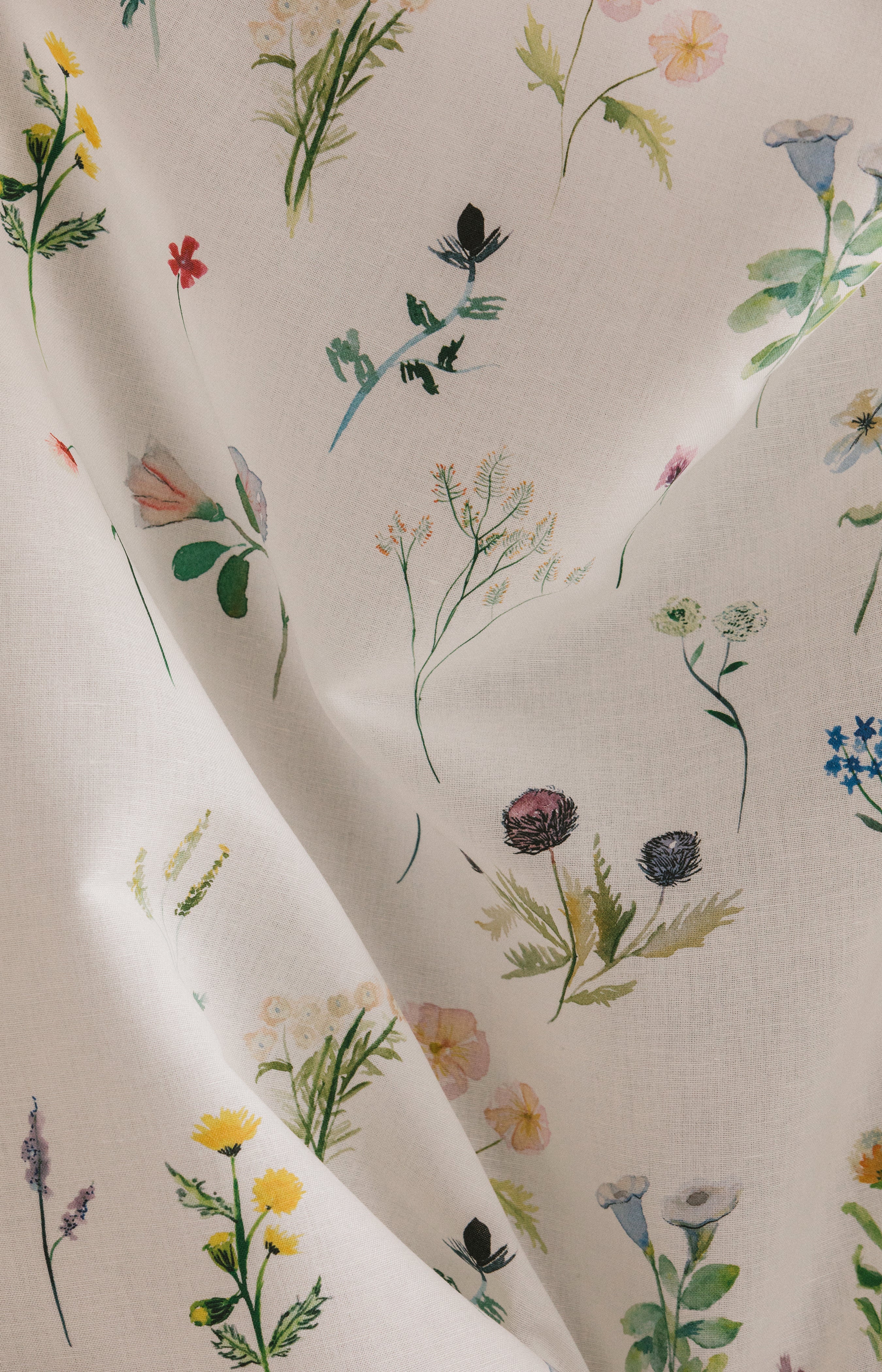 Draped fabric yardage in a painterly flower print in green and pastels on a cream field.