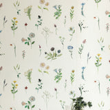 A vase of flowers stands in front of a wall covered in a painterly flower print in green and pastels on a cream field.