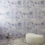 Room interior with a watercolor check wallpaper in blue featuring a white ottoman and small lamp.