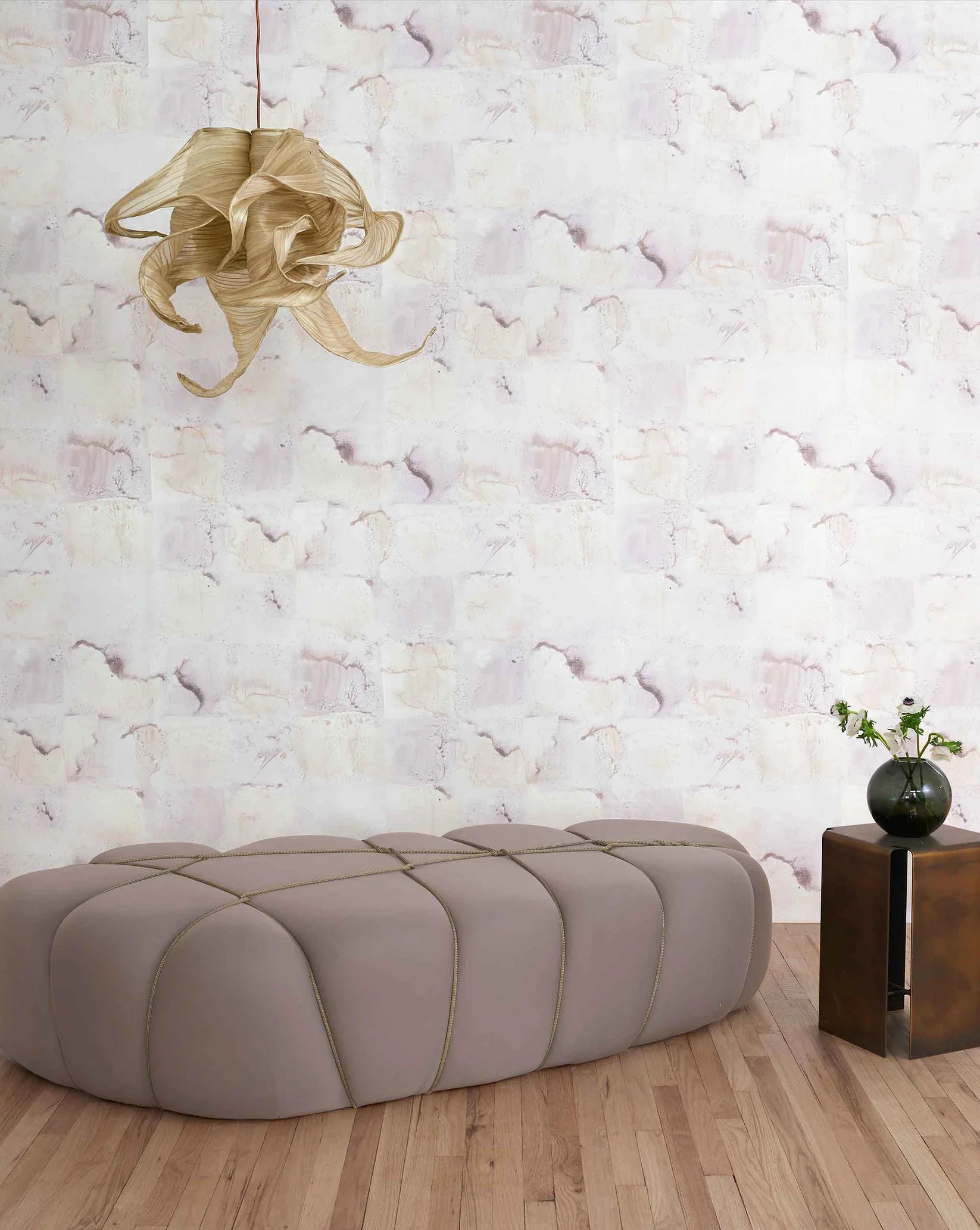 Modern beige ottoman in a room with watercolor check-patterned wallpaper and a decorative light fixture.