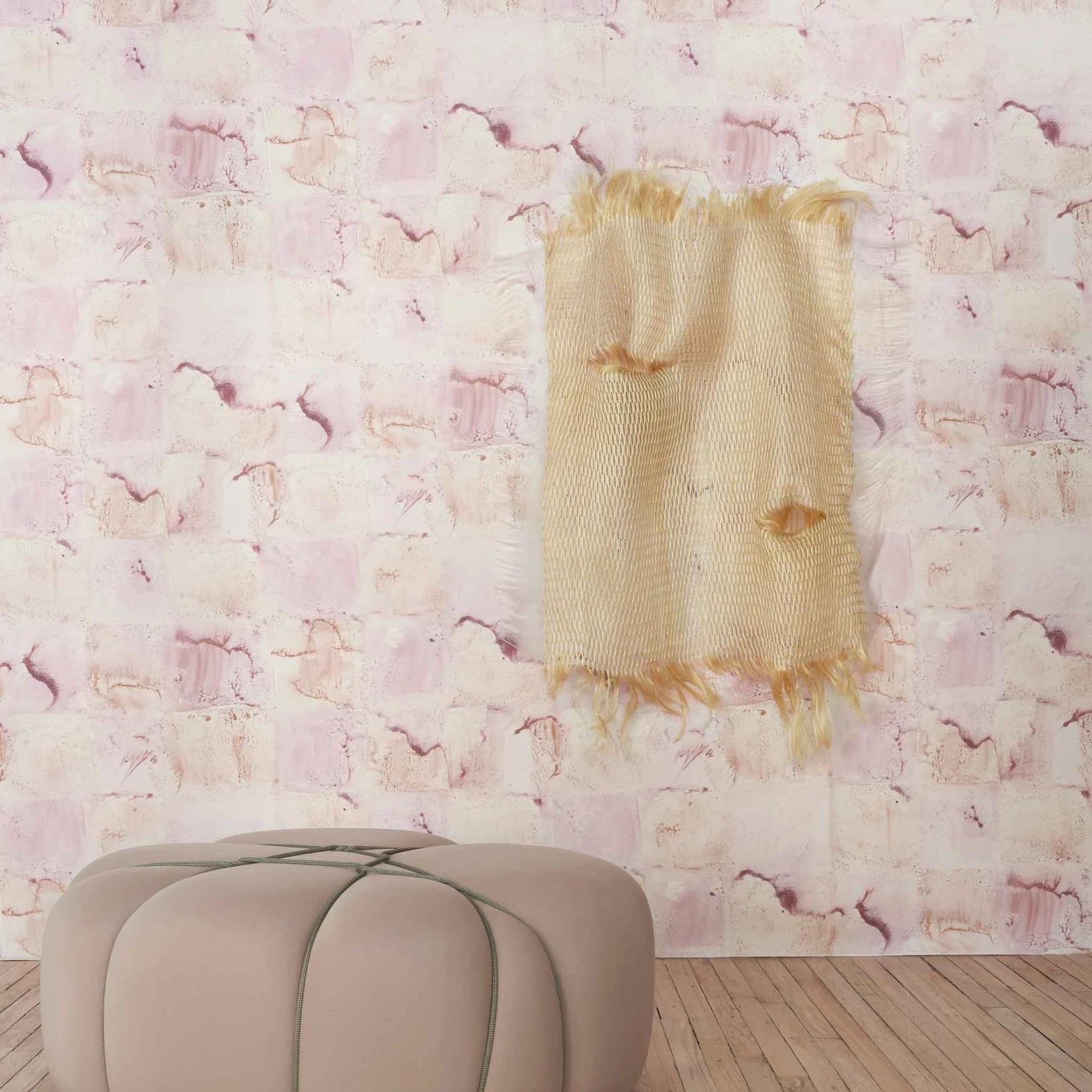 Blush ottoman in front of  watercolor check wallpapered wall in blush.