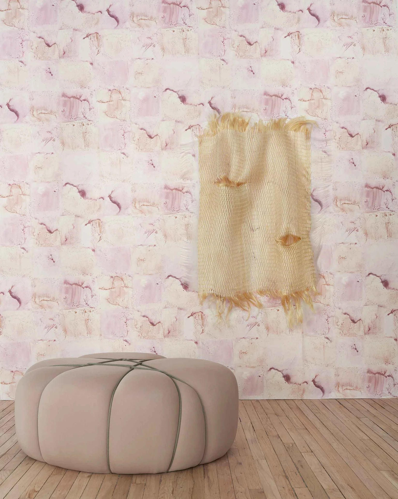 Blush ottoman in front of  watercolor check wallpapered wall in blush.