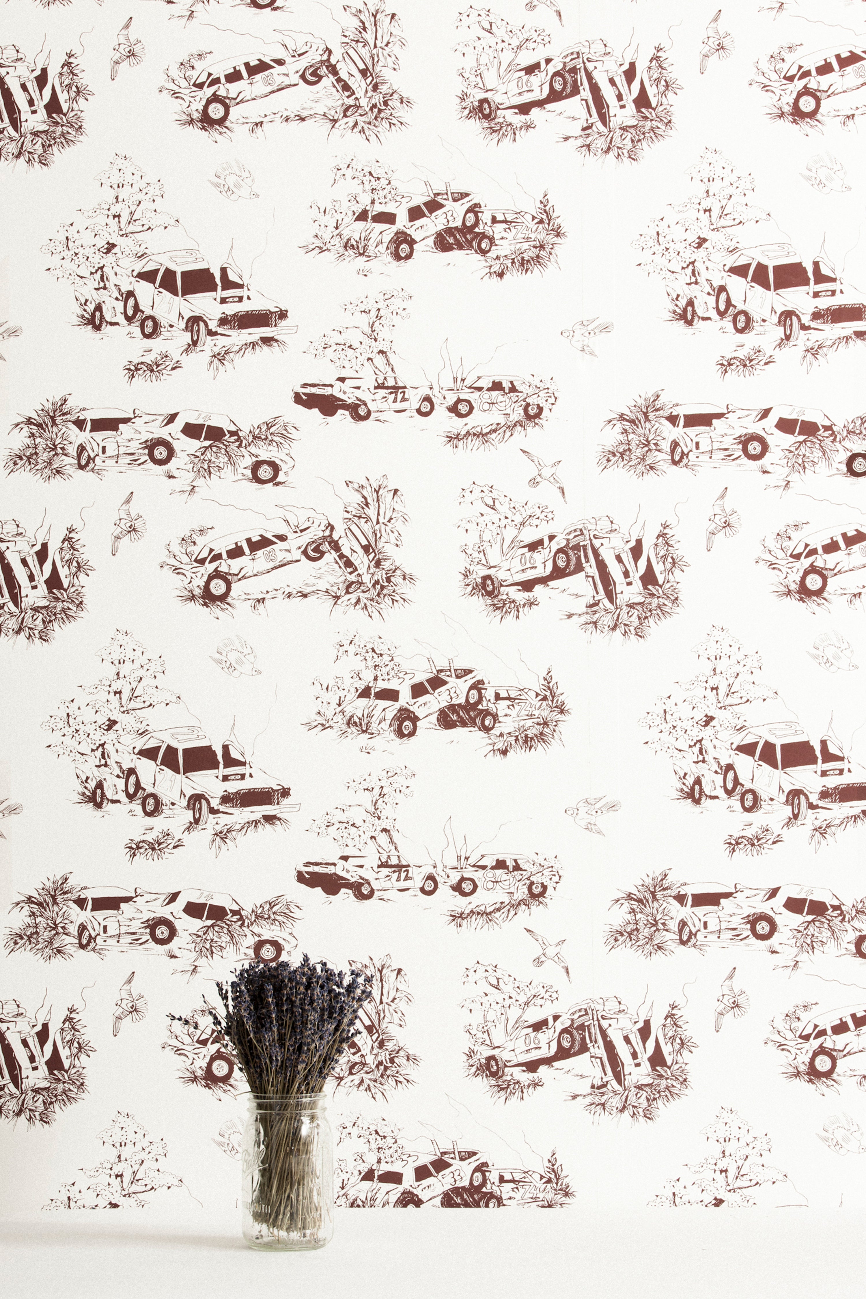 A vase of flowers stands in front of a wall covered in a playful illustrated car crash print in brown on a white field.