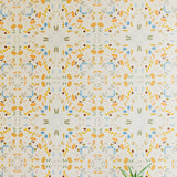 A potted plant stands in front of a wall covered in a painterly grid print in shades of blue and orange on a cream field.