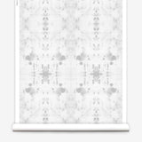 Partially unrolled wallpaper yardage in a watercolor ink blot print in gray on a white field.