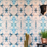 An end table and cactus stand in front of a wall papered in a watercolor ink blot print in blue, gray and light pink.