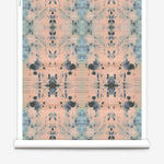 Partially unrolled wallpaper yardage in a watercolor ink blot print in blue and gray on a light pink field.