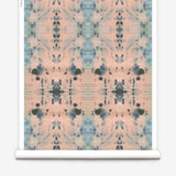 Partially unrolled wallpaper yardage in a watercolor ink blot print in blue and gray on a light pink field.
