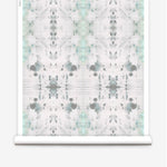 Partially unrolled wallpaper yardage in a watercolor ink blot print in gray and green on a cream field.