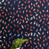 A vase of flowers stands in front of a wall covered in a playful paint blotch print in blue, pink and orange on a navy field.