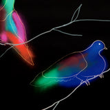 Detail of wallpaper in a painterly bird and branch print in green, yellow, pink and white on a black field.