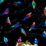 A vase of flowers stands in front of a wall papered in a painterly bird and branch print in green, yellow, pink and black.