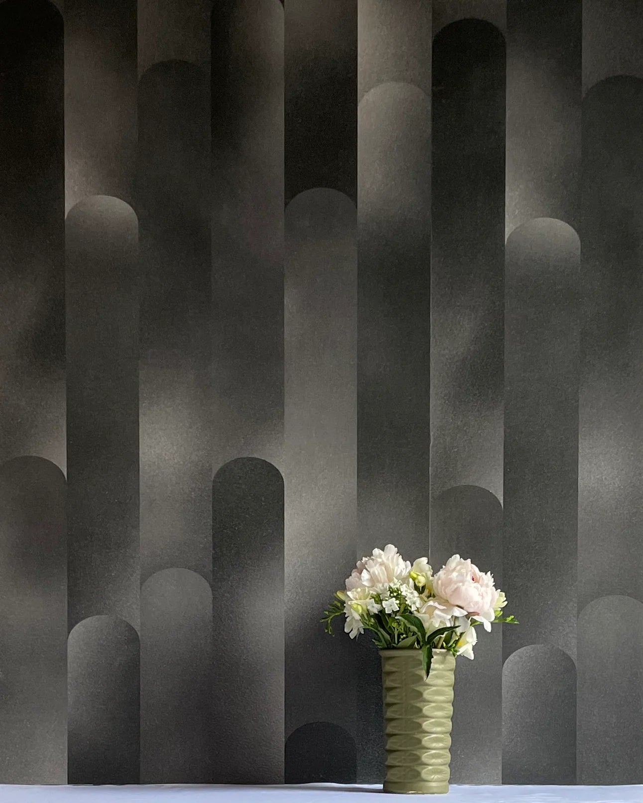 A vase of flowers stands in front of a wall covered in a curvilinear geometric print in shades of black and gray. 