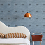 A modernist bed, hanging lamp and chair stand in front of a wall papered in a gridded dash print in black and blue.