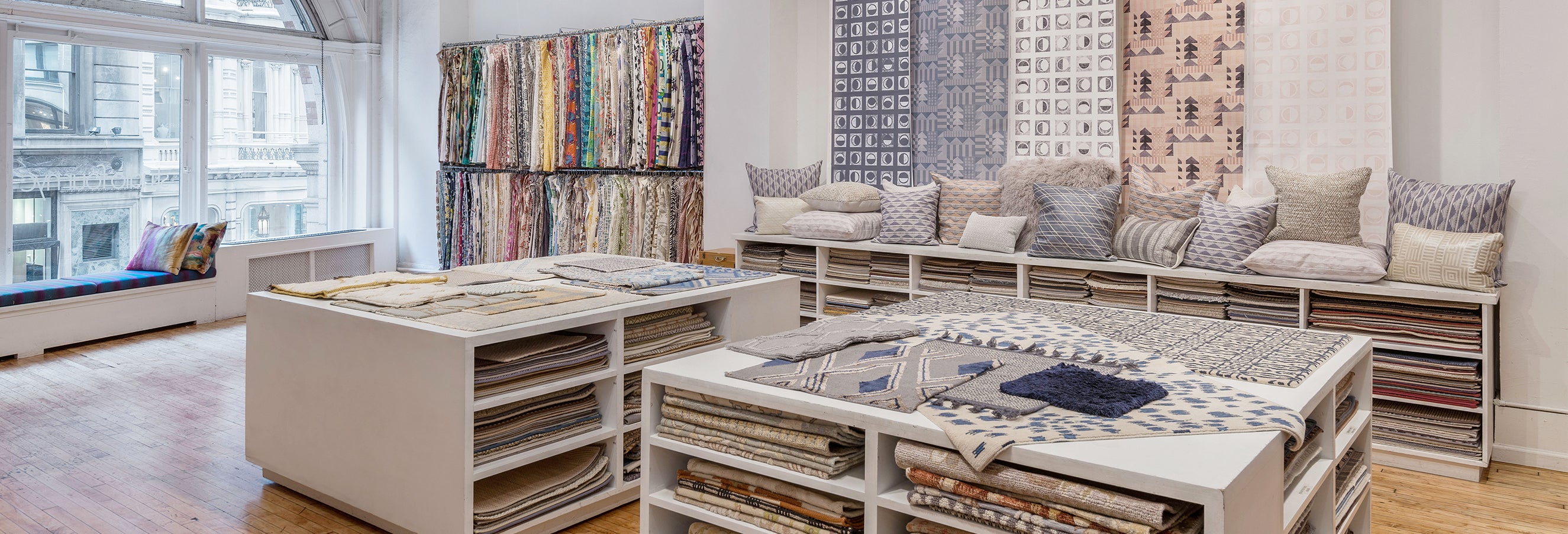 Photo of an airy interior design showroom with hardwood floors, white shelving and walls, and a large curved window.