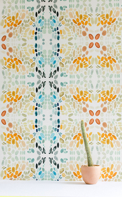 A potted cactus stands in front of a wall papered in a painterly grid print in blue, gray, and orange on a cream field.