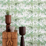 An end table with a plant and sculptures stands in front of a wall papered in a painterly palm tree print in green and white.