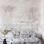 A modernist couch and end table stand in front of a wall papered in a watercolor painterly print in shades of gray and cream.