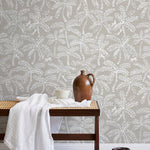 A bench with a towel and clay vases stands in front of a wall papered in a palm tree and monkey print in white and gray.