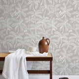 A bench with a towel and clay vases stands in front of a wall papered in a palm tree and monkey print in white and gray.