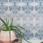 A plant and book stand in front of a wall papered in a watercolor ink blot pattern in shades of gray, blue and pink.