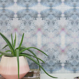 A plant and book stand in front of a wall papered in a watercolor ink blot pattern in shades of gray, blue and pink.