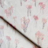 Draped fabric yardage in a painterly palm tree print in shades of pink and gray on a white field.