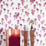 A modernist living tableau with a wall papered in a playful palm tree print in shades of red and purple on a white field.