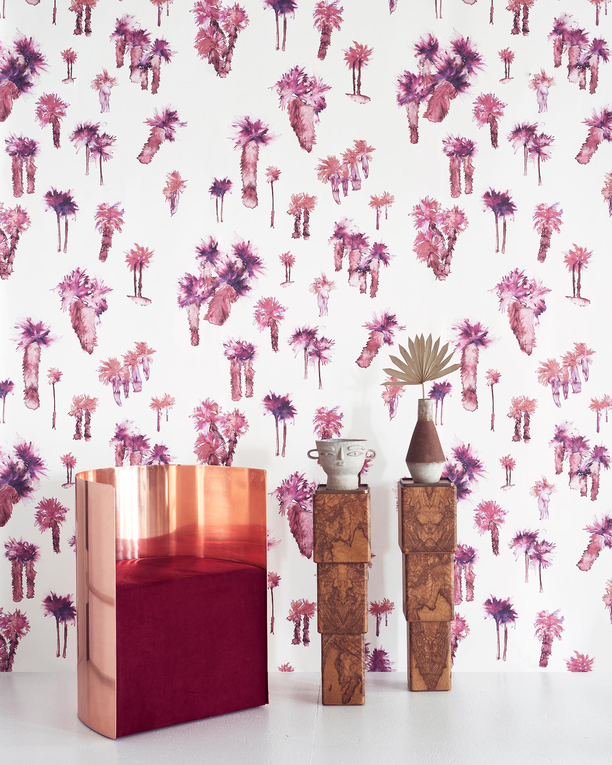 A modernist living tableau with a wall papered in a playful palm tree print in shades of red and purple on a white field.