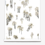 Partially unrolled wallpaper yardage in a playful palm tree print in shades of brown and gray on a white field.