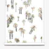 Partially unrolled wallpaper yardage in a playful palm tree print in shades of brown and gray on a white field.