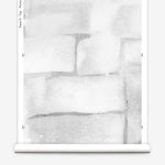 Partially unrolled wallpaper yardage in a watercolor grid print in shades of gray and white.