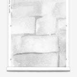 Partially unrolled wallpaper yardage in a watercolor grid print in shades of gray and white.