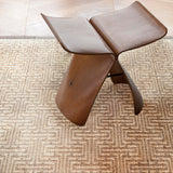 Wooden stool on a geometric stripe area rug in warm brown. 