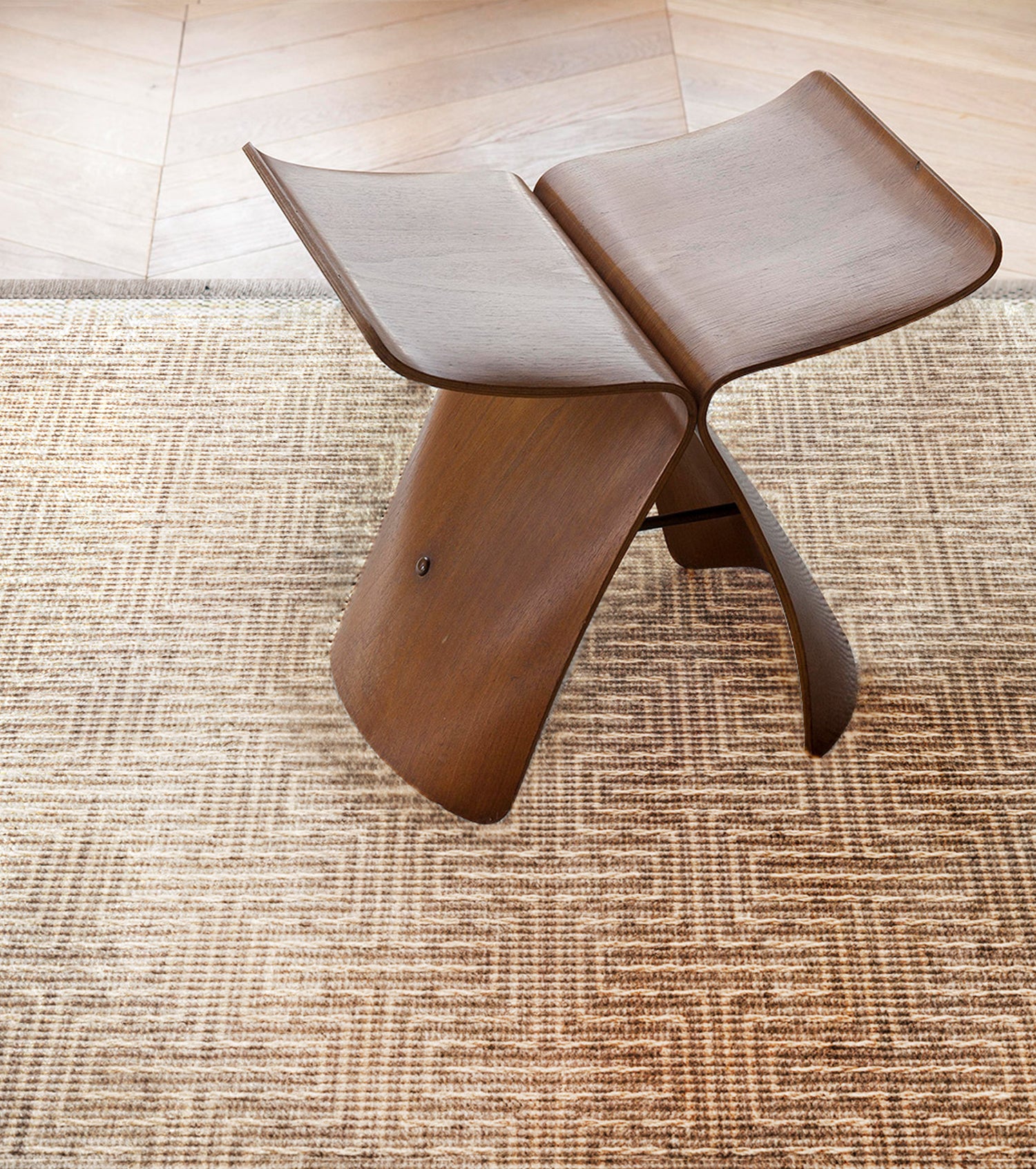 Wooden stool on a geometric stripe area rug in warm brown. 