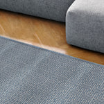 Modern blue couch next to a blue and white striped area rug on a wood floor. 